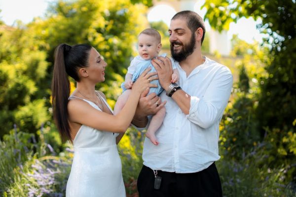 Mother and father joyfully hold their baby in a vibrant outdoor garden setting.